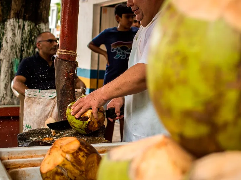 Vendor opening a green coconut with a machete at a street stand