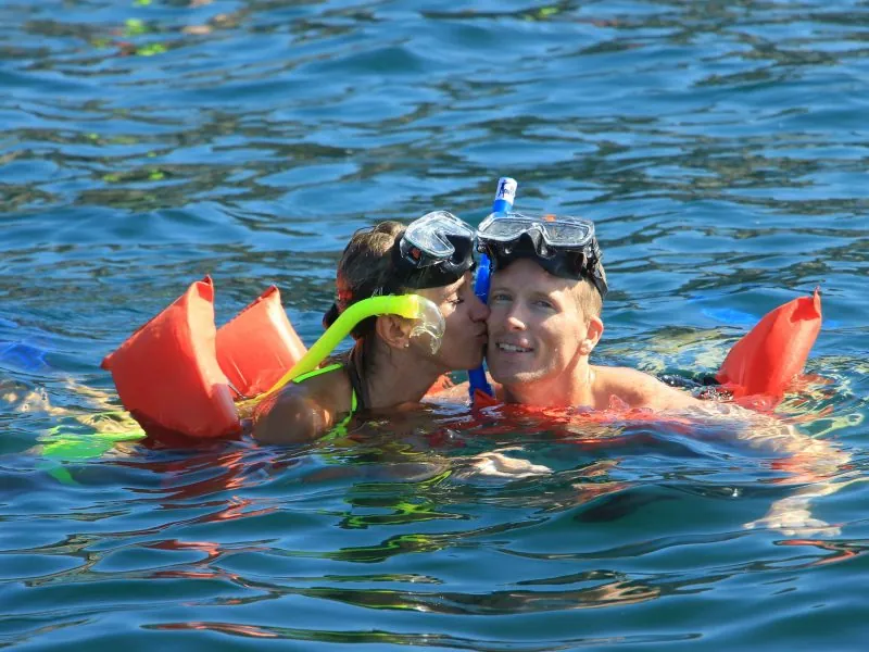 Couple in orange snorkel vests and masks floating together at the surface