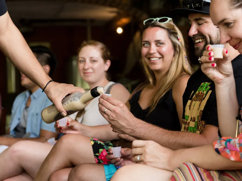 Host pouring from a bottle into small tasting cups for smiling guests