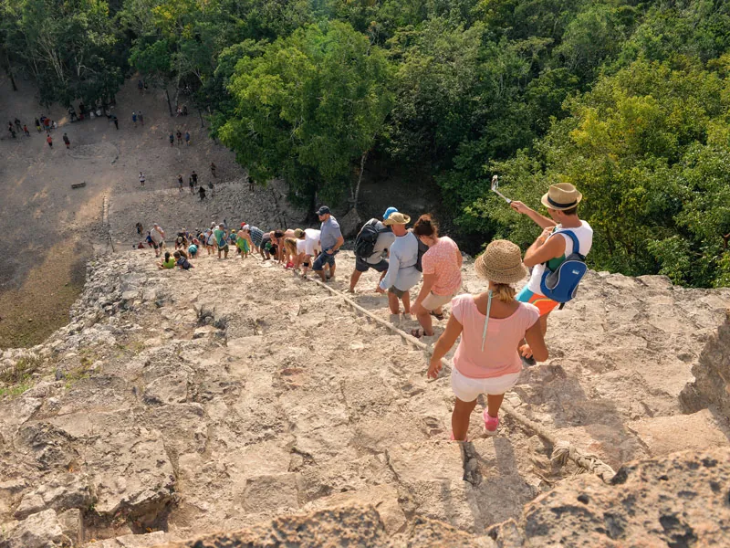 Visitors on the rough stone summit of the pyramid at Cobá, looking down over the forest