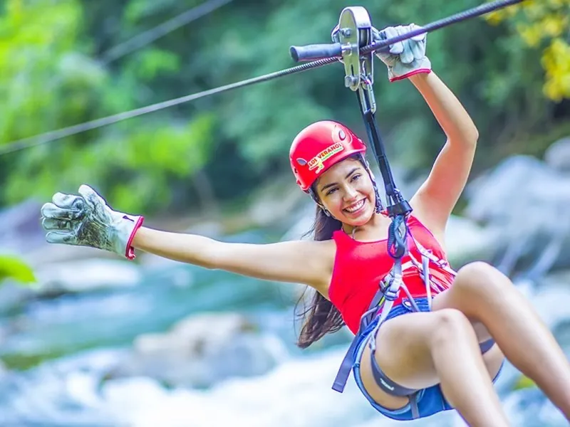 Guest in a red helmet on a zip line with the rapids of the Los Horcones River below at Los Veranos