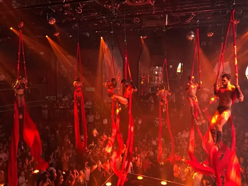 Aerial performers on red silks above the crowd at Coco Bongo in Cancún, lit in red and orange