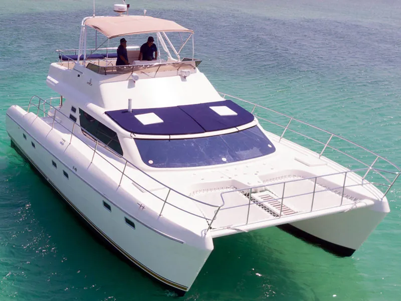 The Africat 44 power catamaran at anchor over green shallows, with two people on the flybridge
