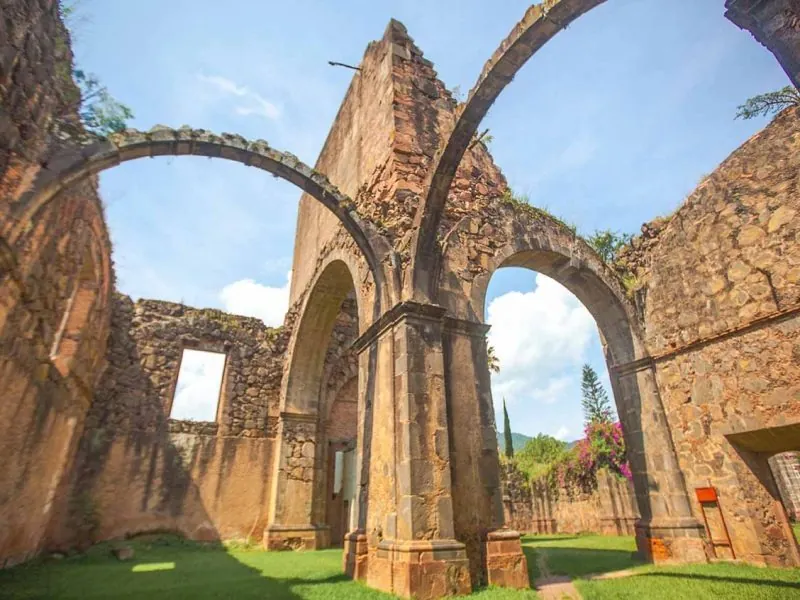 Stone arches of an unfinished church open to the sky, bougainvillea at the base