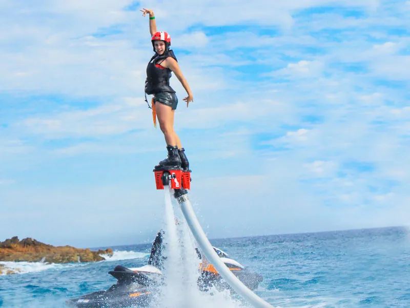 Woman in a helmet flyboarding high over the water with one arm raised