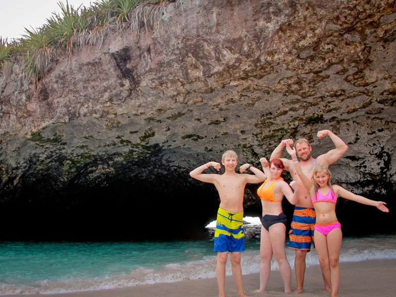 Family posing on the sand in front of the rock arch that leads into the hidden beach