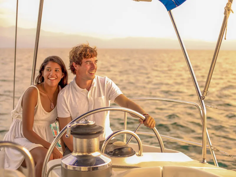 Couple at the wheel of a sailing yacht in warm evening light