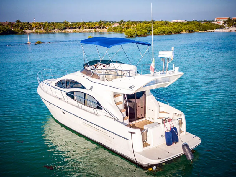 The Azimut 42 flybridge yacht with a blue bimini, anchored in calm blue water near a green shore