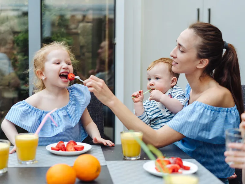 Babysitter feeding two young children breakfast fruit