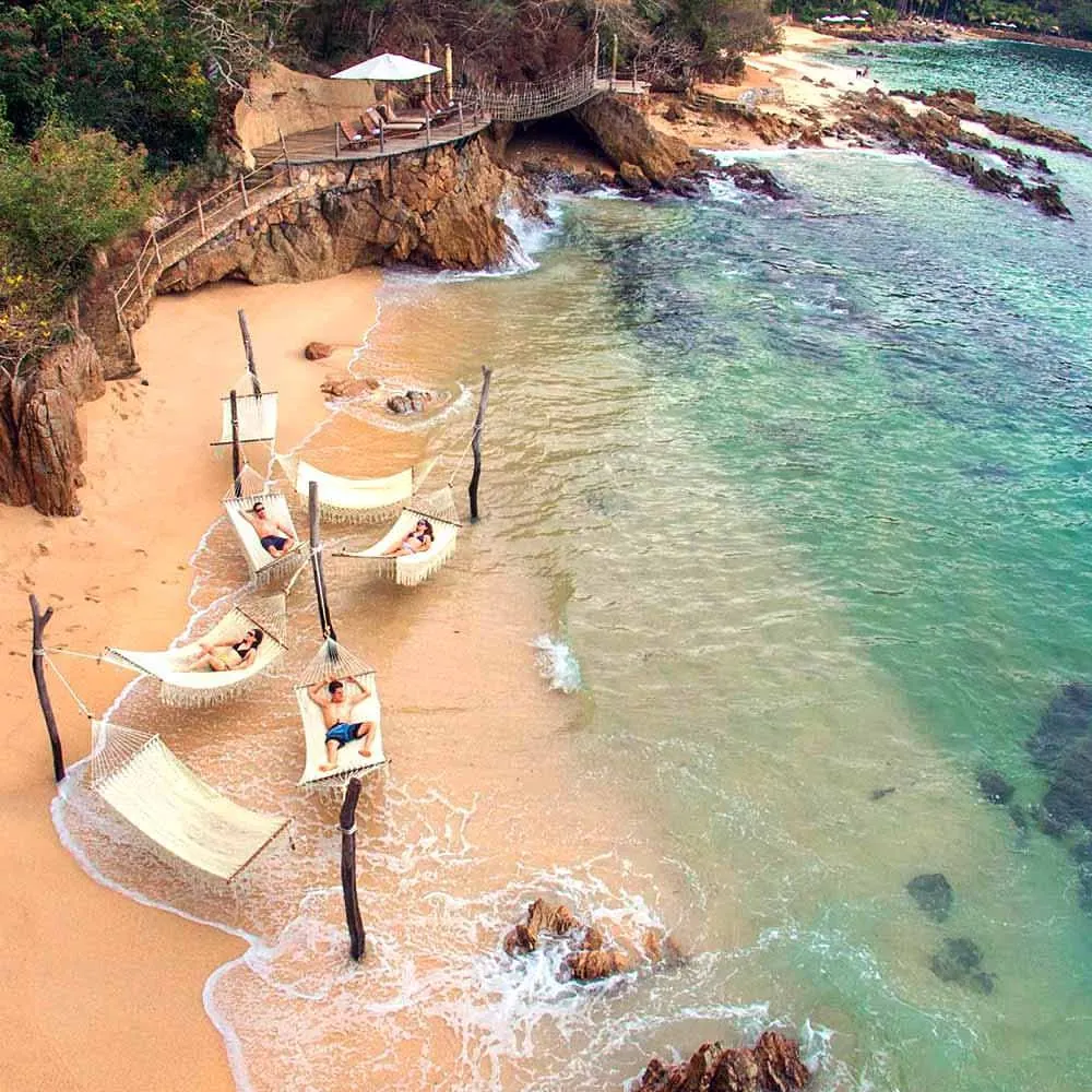 Hammocks strung along the sand at the water’s edge of Las Caletas cove, stone footpath and lookout above