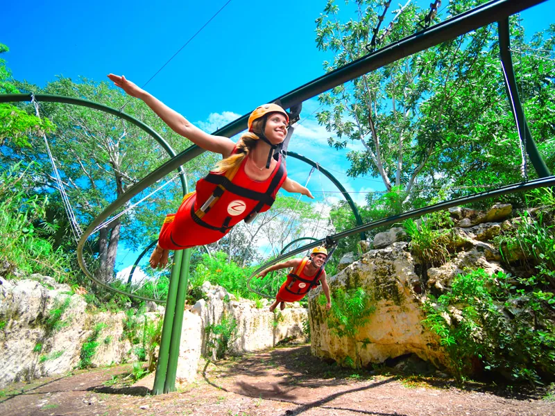 Two guests in harnesses fly face-down along a rail over the trees in the Bird Flight