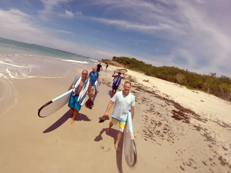 Group carrying surfboards along a wide empty beach on the northern bay