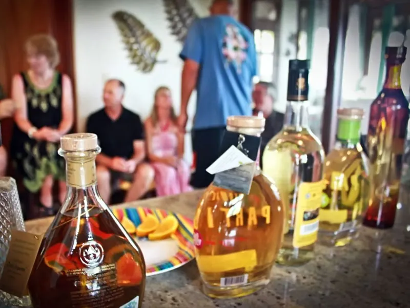 Bottles of añejo and reposado tequila on a counter with orange slices, guests seated behind