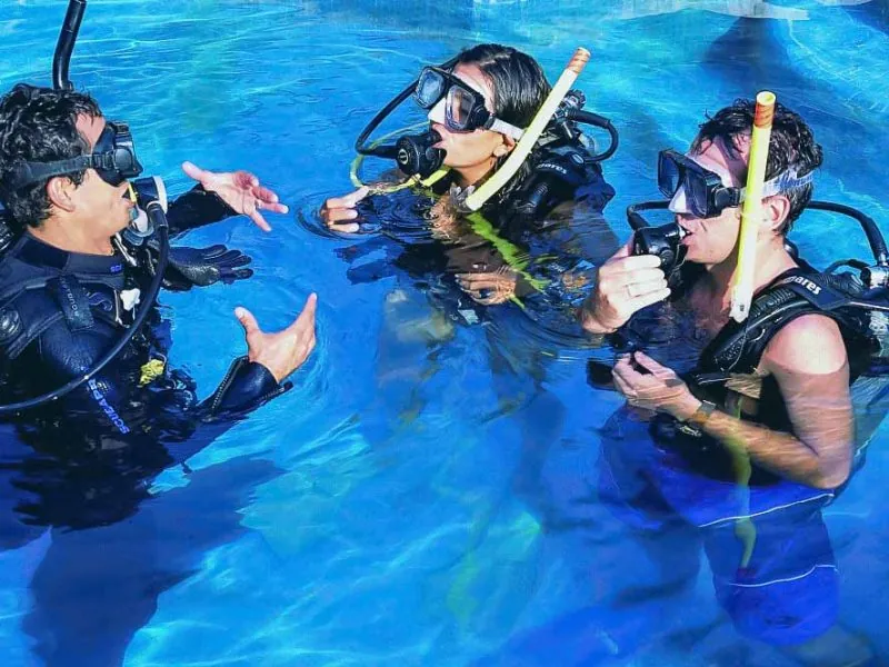 Instructor giving hand signals to two divers at the surface before a beginner dive