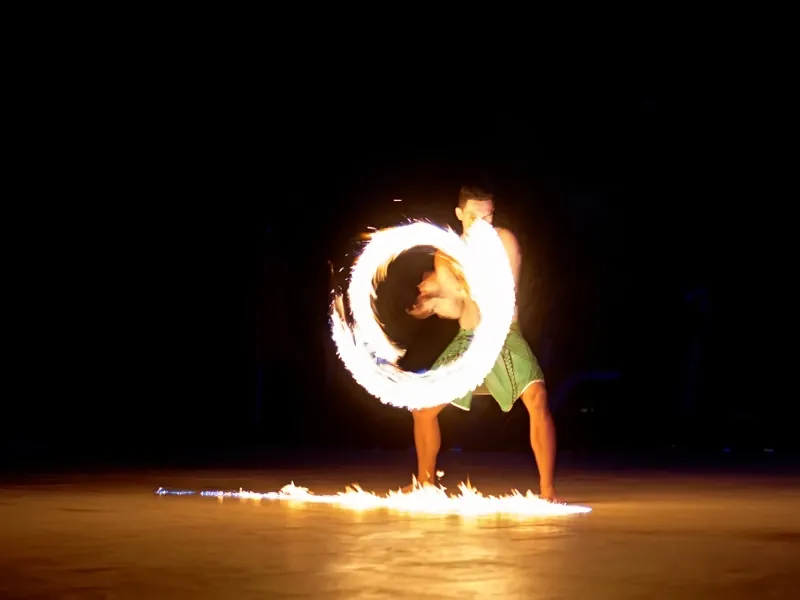 Fire dancer spinning a burning hoop above a trail of flame on the sand
