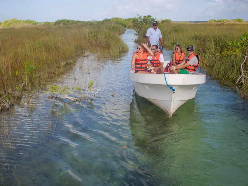 Guests in life jackets on a small boat moving along a narrow canal through tall grass in Sian Ka’an