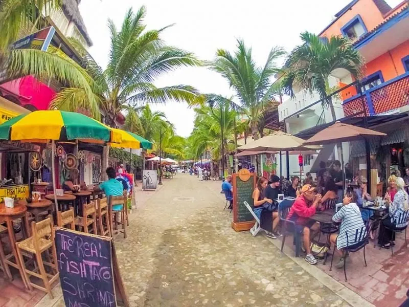 Guests at sidewalk café tables under umbrellas on a sandy street in Sayulita