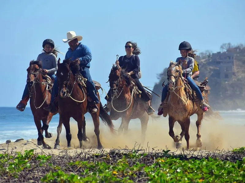 Group of riders cantering along the sand with the Pacific behind them
