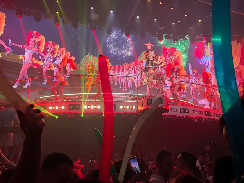 Dancers in feathered carnival costumes performing on a lit stage above the crowd