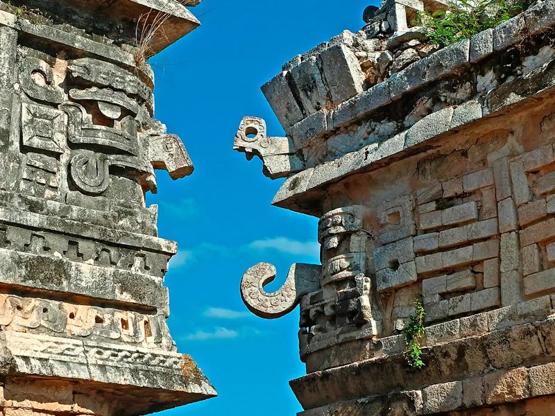 Carved stone masks with curled noses on a Mayan building against a blue sky