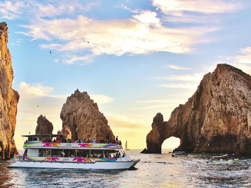 Large catamaran passing the rock arch at Land’s End, Cabo San Lucas, in late afternoon light