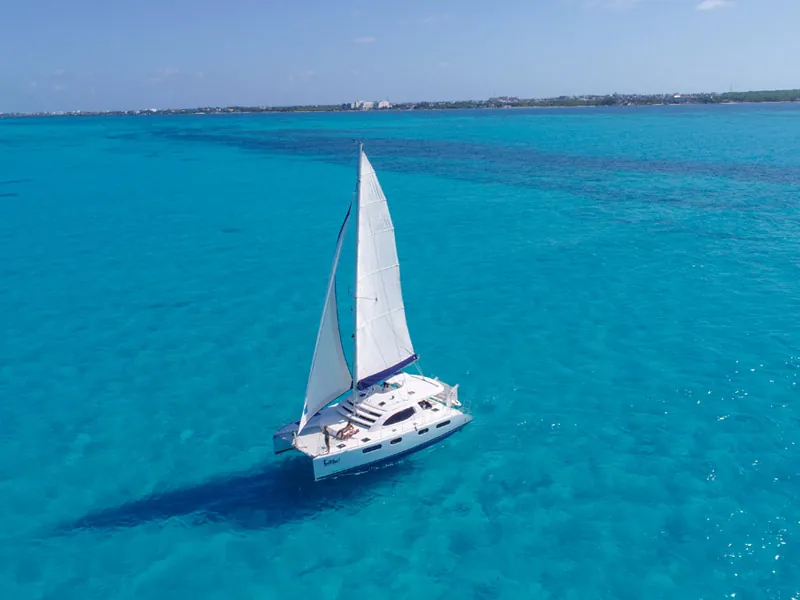 A white sailing catamaran on bright turquoise water between Cancún and Isla Mujeres, seen from above
