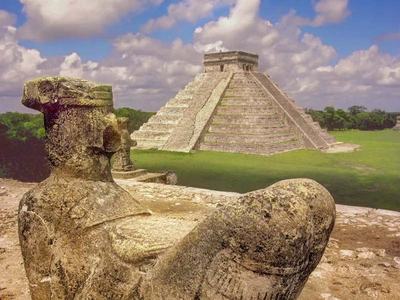 A carved Chac Mool figure in the foreground with the pyramid of El Castillo behind