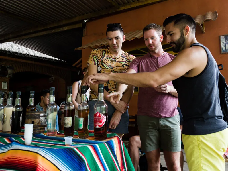 Guests choosing from tequila bottles on a table covered with a striped sarape