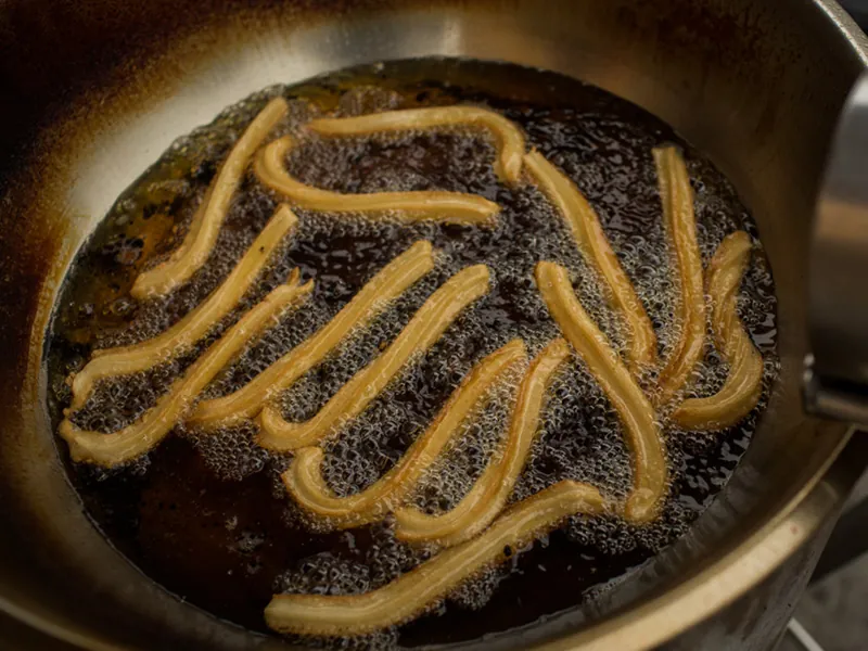 Churros frying in a large pan