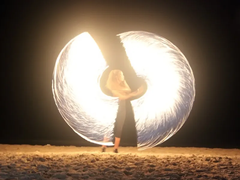 Fire dancer spinning a circle of white flame on a beach at night