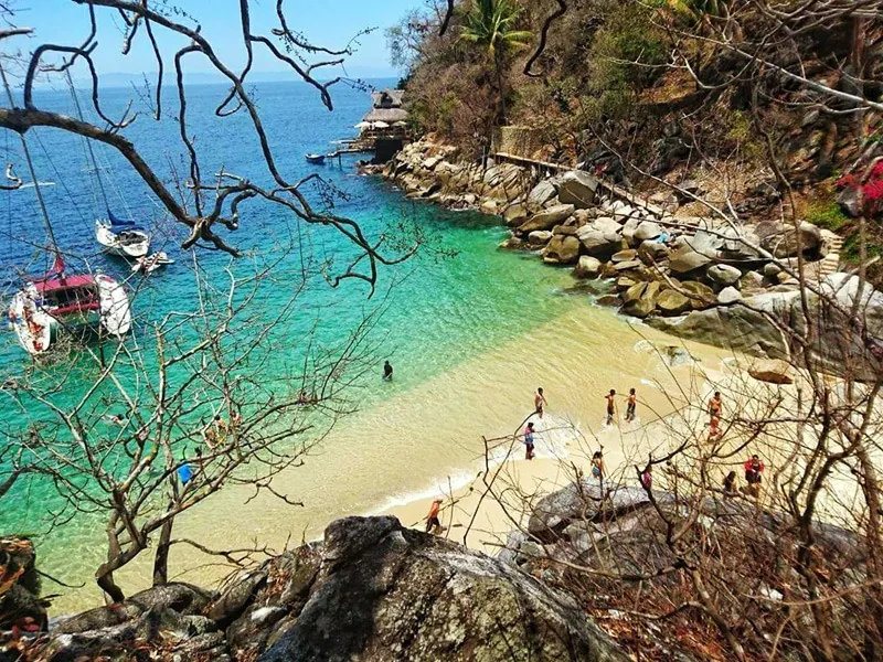 Small cove of Colomitos with turquoise water, a sandy beach and boats moored off the rocks