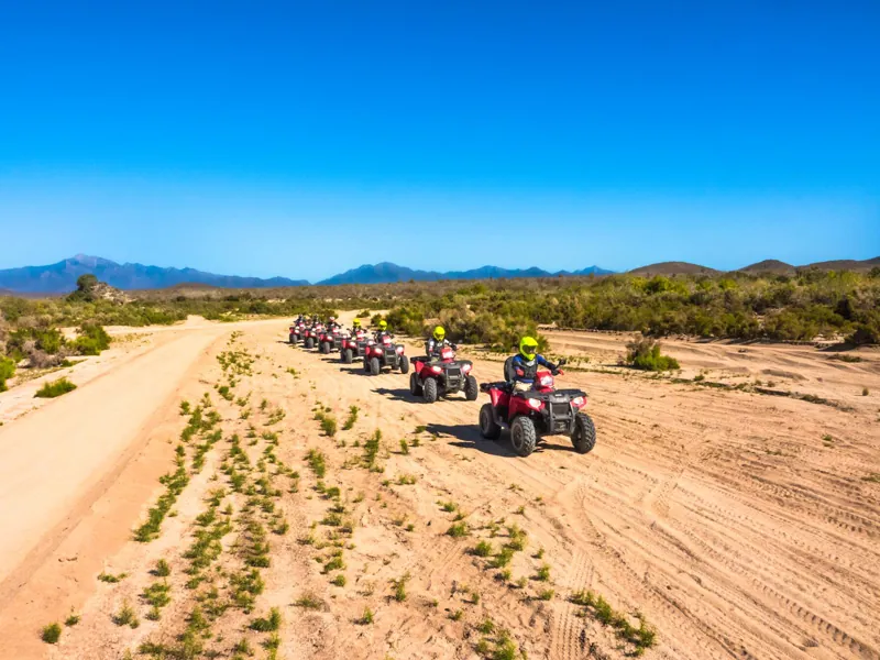 ATV caravan crossing a wide sandy arroyo under a blue sky