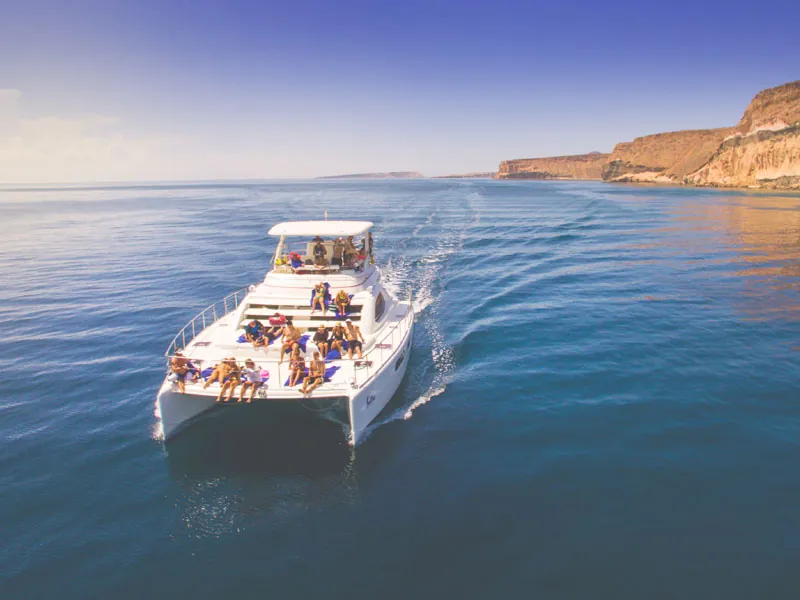 Catamaran with guests on deck cruising past sandstone cliffs