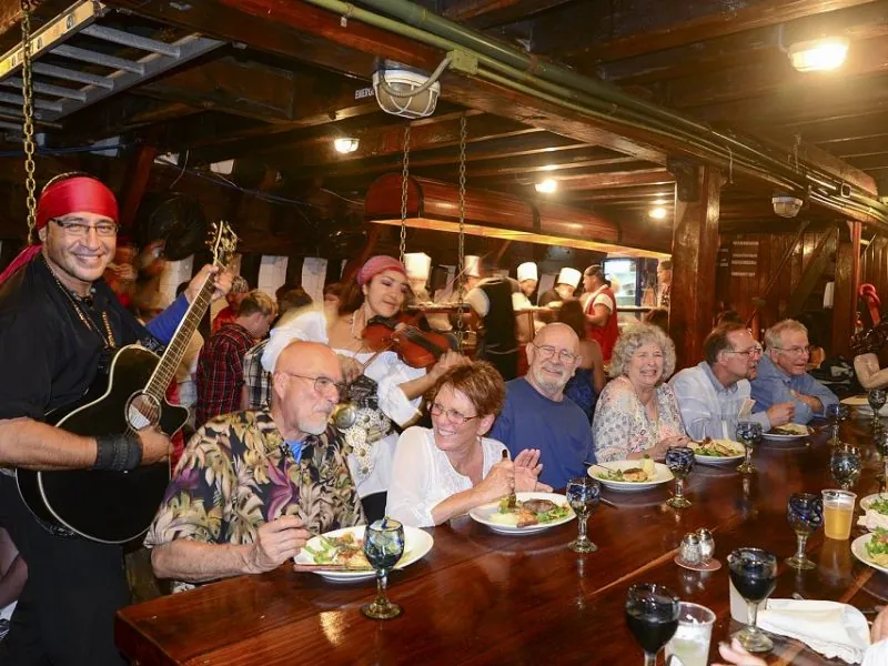 Guests at dinner in the wooden dining room of the ship while a musician plays guitar