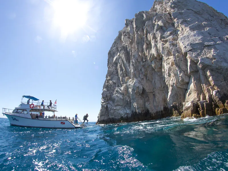 Dive boat beside a sheer granite rock with divers entering the water