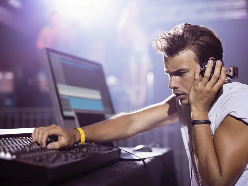 DJ wearing headphones working a console under purple stage lights