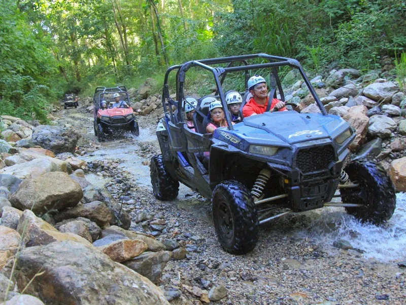 Blue four-seat all-terrain vehicle driving down a rocky stream bed in the jungle near Puerto Vallarta