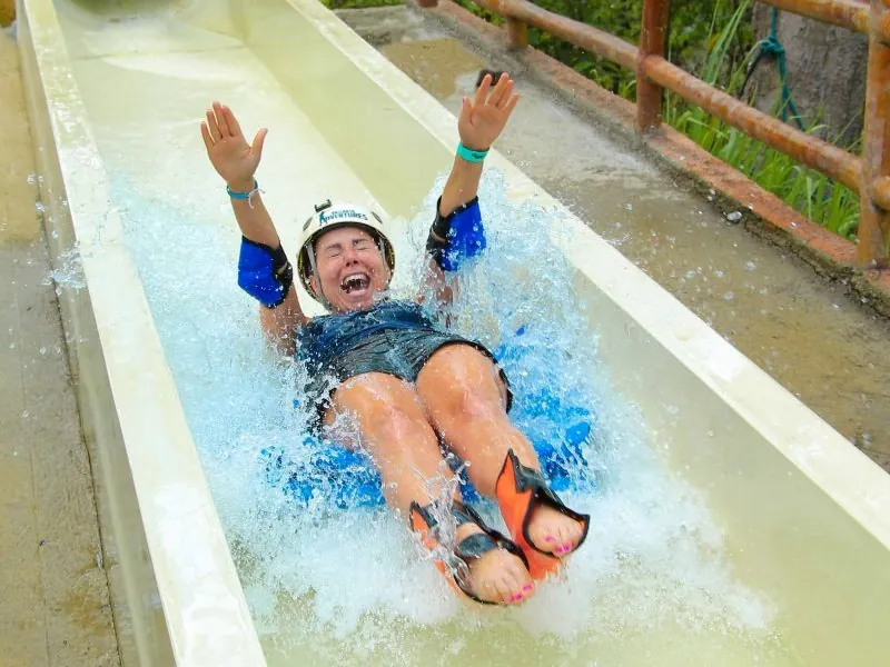 Guest in a helmet sliding down a white water slide with arms raised