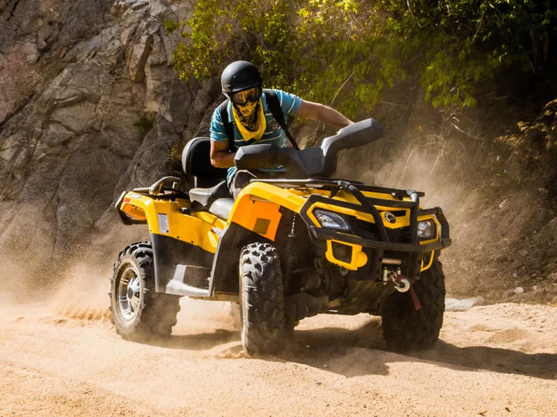 Rider in a helmet and bandana steering a yellow ATV through dust on a mountain trail