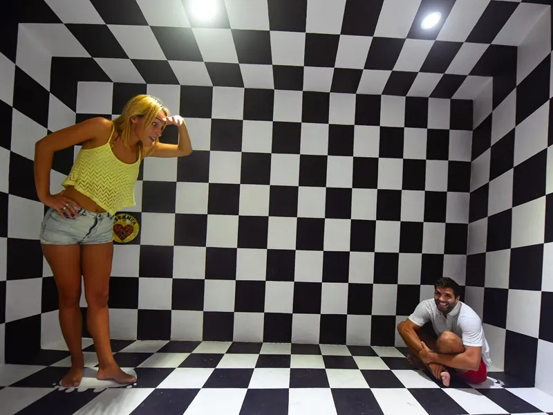 An optical-illusion room of black and white checks makes one guest look huge and one tiny