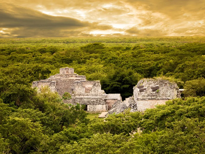Stone temples at Ek Balam rising out of flat green jungle under a golden sky