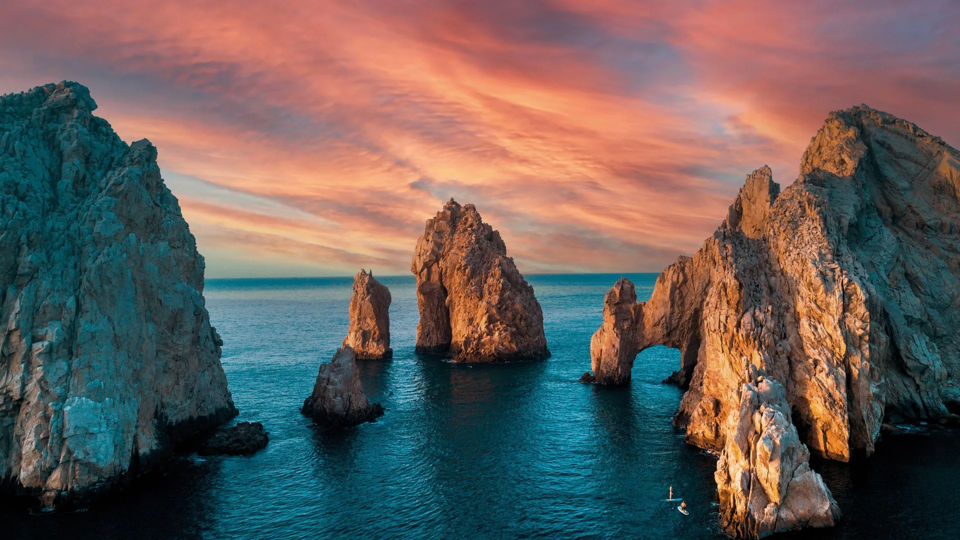 El Arco and the rock pinnacles of Land’s End at sunset, two paddleboarders on the calm water below, Cabo San Lucas