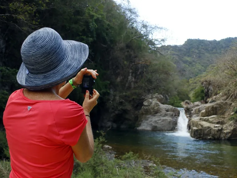 Hiker in a red shirt photographing the El Salto waterfall and its rock pool at El Jorullo