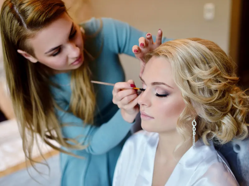 Makeup artist working on a bride’s eye makeup, her hair already styled in loose curls
