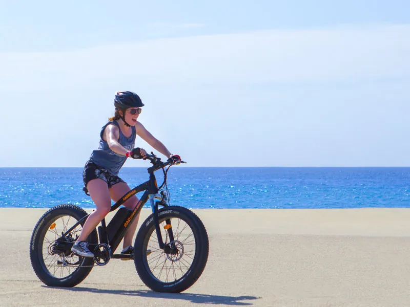Woman riding a black electric fat bike across the sand