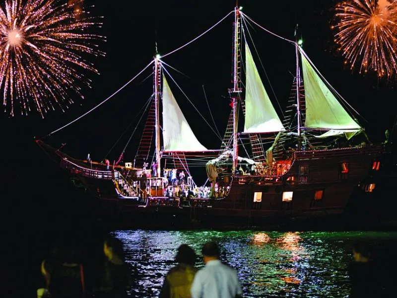 Fireworks bursting over the illuminated pirate ship at night on the bay