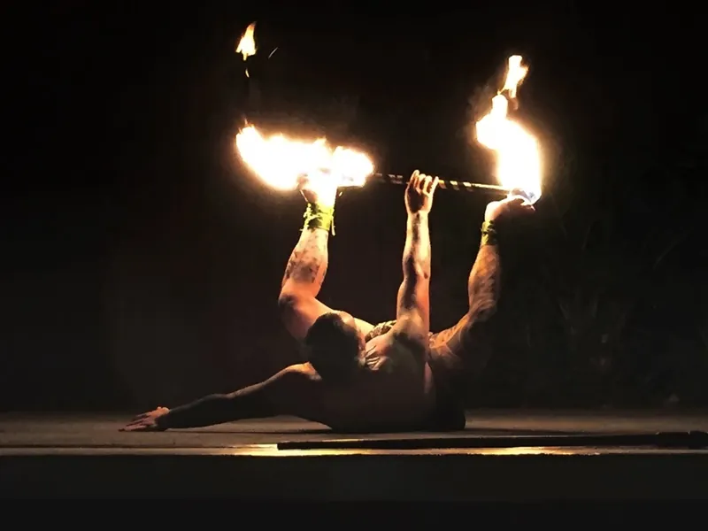 Fire dancer arched backwards holding a flaming staff in the dark