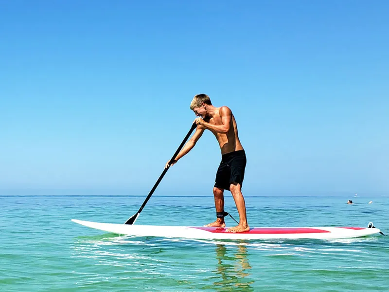 Man paddling a stand-up paddleboard on flat turquoise water under a clear sky