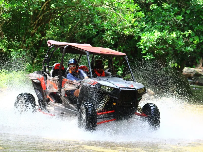 Red RZR throwing spray as it crosses a stream under the trees