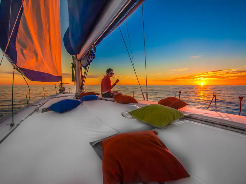 Cushioned sailboat foredeck with a guest watching the sun set over the sea